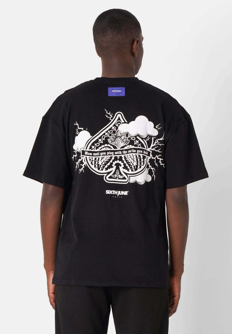 Camiseta de algodón negra con un gran estampado gráfico en la parte posterior que incluye elementos de diseño en blanco, como nubes y texto estilizado, y una etiqueta azul.