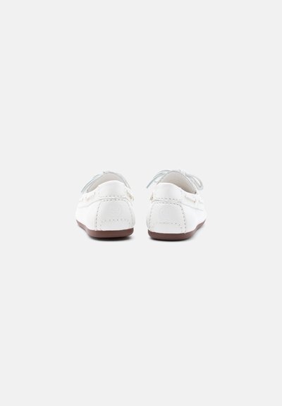 Paire de chaussures décontractées en cuir blanc avec des semelles marron, vues de dos sur un fond gris clair uni.