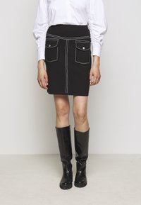 Schwarzer Denim-Minirock mit weißer Stitching, ausgestattet mit zwei Taschen. Kombiniert mit knielangen schwarzen Lederstiefeln. Glatte Textur, taillierte Passform.