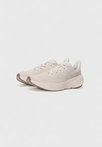Light beige athletic shoes with a breathable mesh upper, cushioned midsole, round toe, and textured rubber outsole. Features laces and logo.