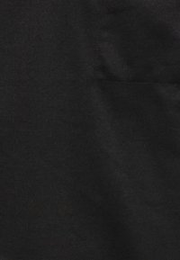 Czarna tkanina z wyszywaną kwadratową kieszenią po prawej stronie, ukazująca teksturę i lekkie zmarszczki w okolicy kieszeni.