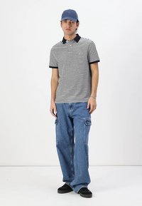 Striped polo shirt with navy collar, blue cargo jeans, and black sneakers. Accessories include a light blue cap and silver bracelets.