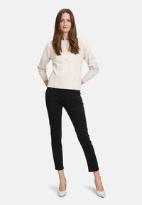 Světle béžový textured svetr s dlouhými rukávy, doplněný černými slim-fit kalhotami a bílými lodičkami s špičatou špičkou. Jednoduchý, elegantní design.