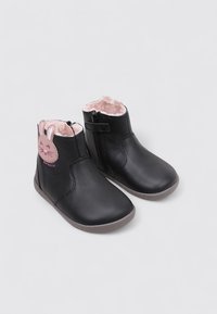 Botas de cuero negro con un forro de piel de conejo rosa, un diseño de cara de conejo en el lado y una cremallera lateral para ponerlas y quitarlas fácilmente.
