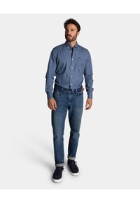 Blauw button-up overhemd met een klein wit stippenpatroon, gecombineerd met medium-wash jeans en donkere sneakers. Casual pasvorm met lange mouwen.