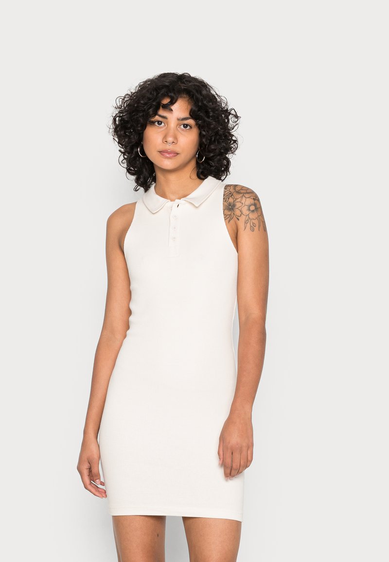 Vestido sem mangas em bege com gola. Apresenta um fechamento com botões e um formato justo. Textura suave e corte até ao joelho.