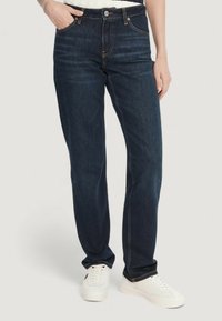 Mørkeblå denimjeans med lige ben, fem lommer og kontrastsyning, kombineret med hvide sneakers.