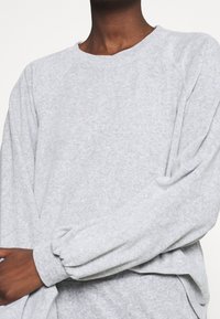 Sudadera gris de algodón con mangas largas raglán, corte relajado, puños acanalados y cuello redondo. Textura suave y coloración uniforme.