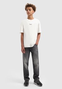 Witte katoenen t-shirt met "BALLIN'" logo, gecombineerd met grijze denim jeans. Schoenen hebben een zwart-wit ontwerp met textuuraccenten.