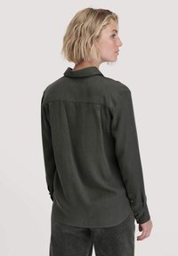 Camicia a maniche lunghe di colore verde scuro con colletto e polsini abbottonati, dalla texture liscia e dettagli sul dorso.
