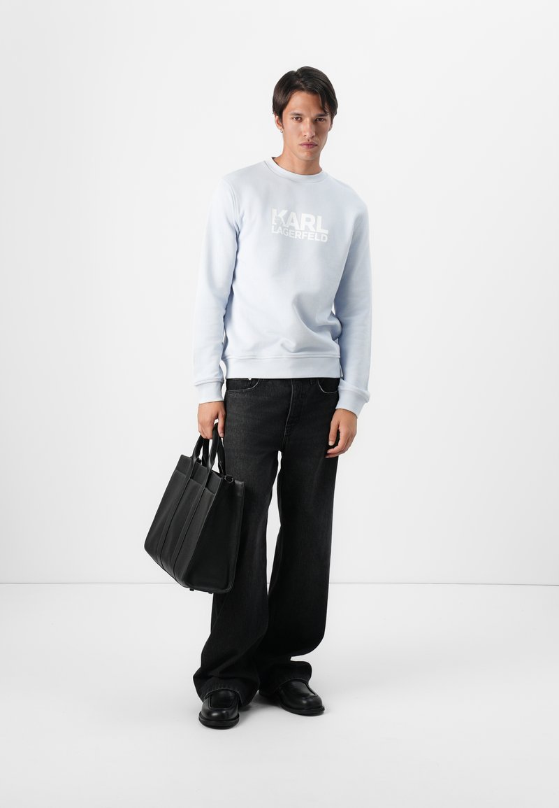 Sweat-shirt bleu clair avec le logo blanc "KARL LAGERFELD", associé à un jean large noir et un sac fourre-tout noir, présentant des poignées doubles.
