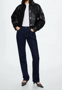 Zwarte leren cropped jas met twee voorzakken, gecombineerd met donkerblauwe rechte jeans en zwarte hoge hakken met versieringen.