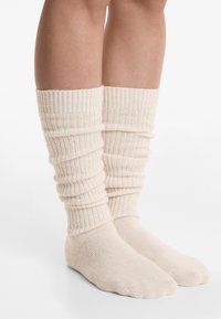 Knæhøj ribbede sokker i lys beige, med foldede toppe og en hyggelig tekstur. Materialet ser tykt og varmt ud for komfort.