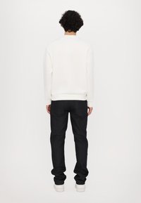 Hvid sweatshirt med ribbestrikkede manchetter og afslutning, parret med mørke denimjeans. Stoffet ser glat ud, og jeansene har en klassisk pasform.