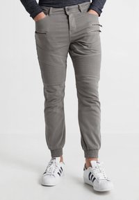 Graue elastische Hosen mit gerippten Nähten und Reißverschlusstaschen, kombiniert mit weißen Sneakers mit schwarzen Streifen.
