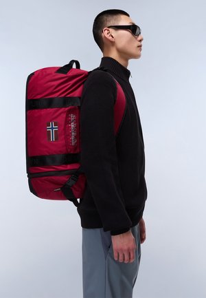 Red backpack with black straps, logo, and Norwegian flag patch. The backpack is rectangular, made of shiny material, worn over a black sweater.