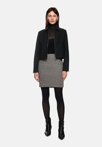 Schwarze cropped Jacke über einem schwarzen Top, kombiniert mit einem gemusterten Rock in Schwarz und Weiß. Getragen mit schwarzen Strumpfhosen und Stiefeletten.