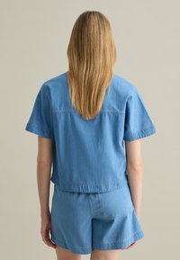 Top di denim azzurro chiaro con maniche corte e vestibilità rilassata, abbinato a pantaloni corti nello stesso azzurro chiaro. Texture liscia e dettagli di cucitura semplici.
