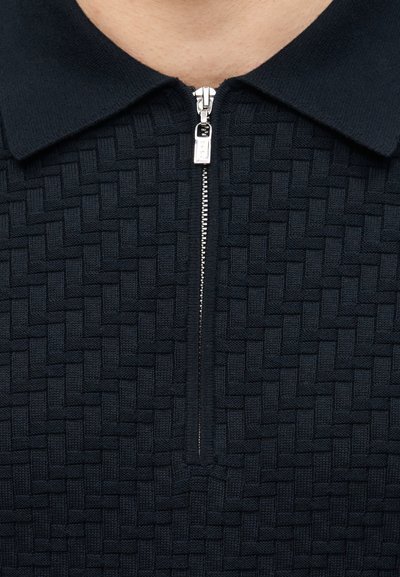 Κοντινή λήψη σε υφασμάτινη πλεκτή υφή ναυτικού μπλε με μοτίβο πλεκτού καλαθιού, ασημένιο φερμουάρ μερικώς κλειστό κάτω από γιακά σε ένδυμα.