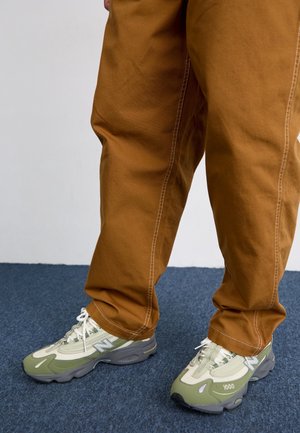 Jasnozielone i szare sneakersy New Balance z siateczkowej i teksturowanej tkaniny, białymi sznurówkami i szarym spodem. Dobrane do beżowych, luźnych spodni.