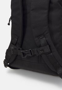 Sac à dos noir en tissu durable, avec des bretelles ajustables, des fermetures en plastique et un design épuré avec un minimum de décorations.