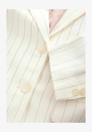 Blazer blanco a rayas con líneas negras, con botones claros y una tela suave y texturizada. Incluye un detalle de bolsillo en la solapa.