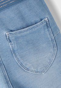 Light blue denim fabric featuring a small patch pocket with a rounded shape and contrasting white stitching along the edges.