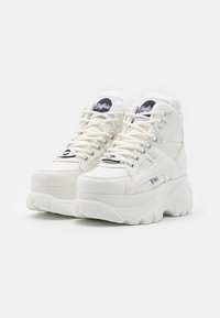 Baskets montantes blanches avec une semelle épaisse, en matériau synthétique lisse, bout rond et patch logo noir sur la languette. Semelle extérieure texturée.