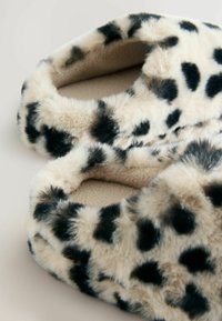 Chaussons à motifs léopard avec un extérieur en fausse fourrure douce, doublure en peluche, forme arrondie et surface texturée, ornés de taches noires sur un fond beige.