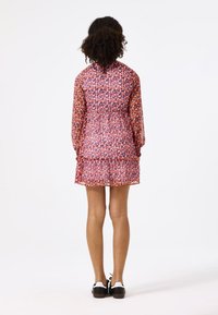 Vestido floral con mangas largas, tejido ligero, dobladillo con volantes y tonos rojos/púrpuras, combinado con zapatos negros con acentos blancos.