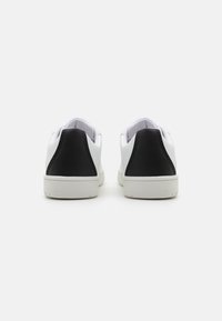 Baskets blanches avec des accents noirs au niveau du talon, en matériau synthétique lisse, de forme arrondie et avec des semelles en caoutchouc blanc. Design minimaliste sans motifs.