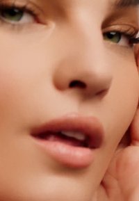 Primer plano de una cara con piel suave, labios rosa claro y ojos verdes. La luz suave resalta las características naturales y la textura de la piel.