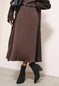 Hnědé žebrované pletené midi šaty, doplněné dlouhým hnědým kabátem. Černé semišové kotníkové boty na blokovém podpatku. Černý kožený opasek a kabelka.