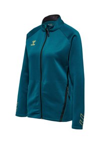 Sportsjakke i teal med lynlås, ståkrave, sorte lynlåse, sidelommer med lynlås og gult logo samt Chevron-detaljer på fronten og ærmerne.