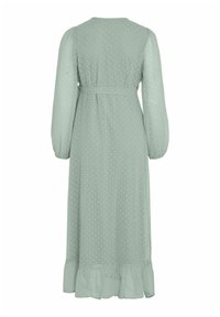 Lang mintgrønn kjole med prikkete tekstur, samlet lange ermer, innsnevret midje og volangkant. Lett, flytende stoff.