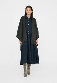 Donkergrijze sjaal met franjes, gedragen over een denim jurk met knopen aan de voorkant en een uitlopende rok, gecombineerd met gebloemde kniehoge laarzen.