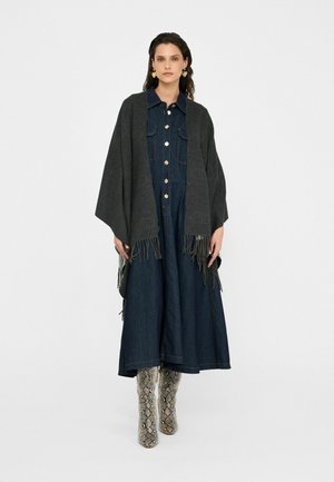 Dark gray shawl with fringe overlay, worn over a denim dress with a button front and flared skirt, paired with patterned knee-high boots.