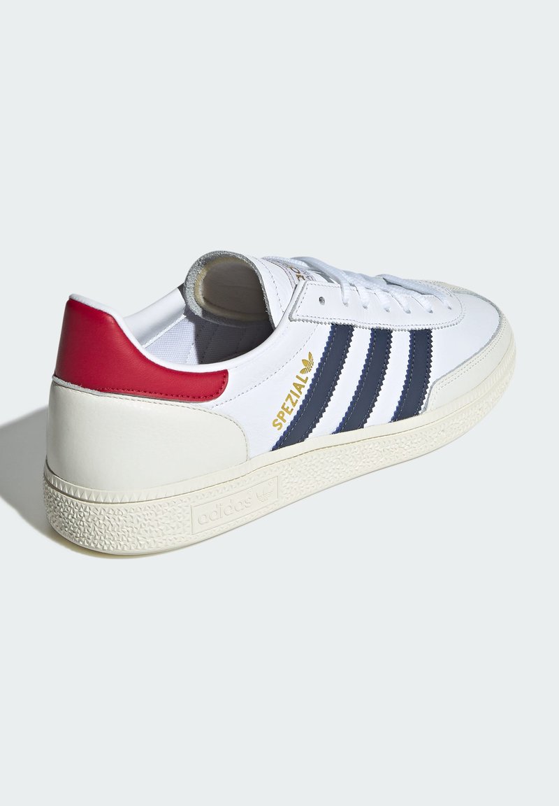 Białe skórzane sneakersy z granatowymi paskami, czerwonym akcentem na pięcie, teksturowaną gumową podeszwą i złotymi detalami "Spezial" na boku.