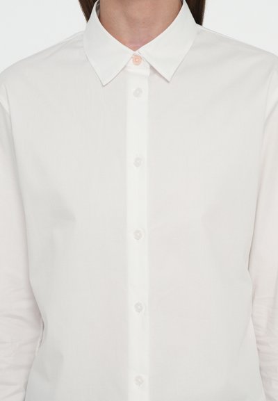 Camicia button-up in cotone bianco con colletto classico, caratterizzata da una fila di bottoni sul davanti e una texture liscia e resistente alle pieghe.