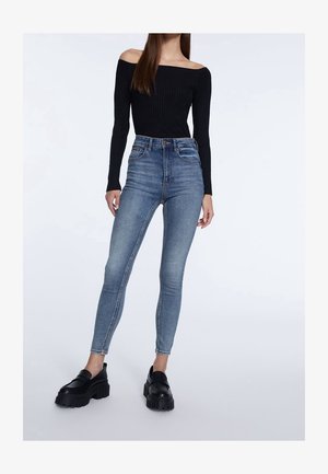 Top nero a costine off-shoulder con maniche lunghe abbinato a jeans skinny azzurri a vita alta e mocassini neri chunky.