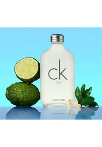 Calvin Klein CK One doftflaska, frostad glas med silverlock, omgiven av halverad lime, limer, färska blad och bergskristaller.