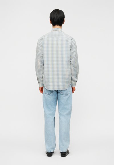 Πουκάμισο με καρό σχέδιο, μακρυμάνικο, σε ανοιχτό μπλε και λευκό χρώμα, με ευθεία γραμμή και γιακά με κουμπιά. Συνδυάζεται με ανοιχτό μπλε τζιν και μαύρα παπούτσια.
