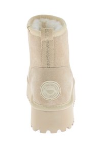 Bota de ante beige con punta redondeada, que presenta un acabado texturizado, un suave forro de piel y un logotipo circular en la parte trasera. La suela es gruesa.