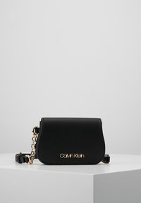 Sort syntetisk håndtaske med rund form, guldfarvede beslag, kæderem og præget logo foran.