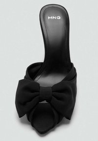 Zapato de satén negro tipo slip-on con punta abierta, que presenta un gran lazo en la parte delantera y una silueta elegante y puntiaguda. El logo de MNG es visible en la plantilla.