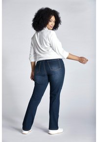 Dunkelblaue Jeans im Slim-Fit mit Rückentaschendetail, kombiniert mit einem weißen Oberteil mit drei Viertelärmeln. Das Modell posiert von hinten.