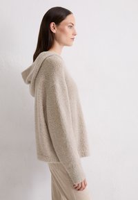 Felpa con cappuccio in morbido beige, caratterizzata da una finitura testurizzata, vestibilità comoda e un cappuccio discreto. Design semplice senza loghi visibili.