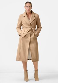Beige wollen blend lange jas met een geknipte kraag, voor knopen, strik taille en zijzakken, gecombineerd met licht beige enkellaarsjes.