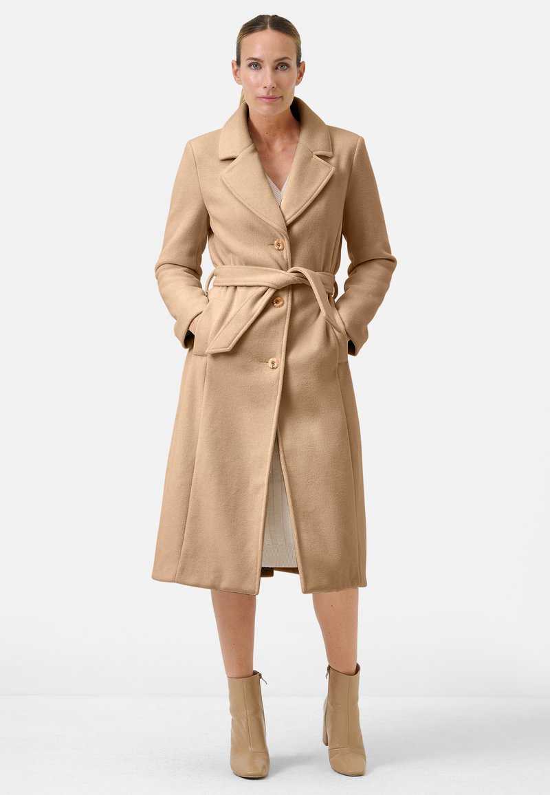 Beige wollen blend lange jas met een geknipte kraag, voor knopen, strik taille en zijzakken, gecombineerd met licht beige enkellaarsjes.