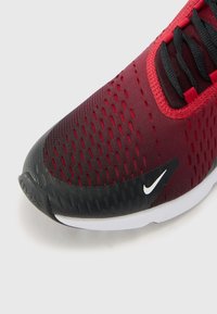 Červená a čierna športová obuv s vrchom z jemnej sieťoviny, textúrovanou čiernou špičkou a bielym logom Nike swoosh.